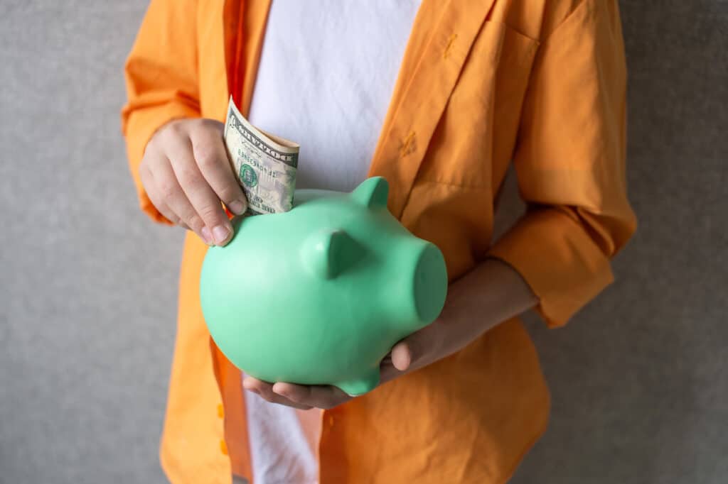 Piggy bank in the hands of a child. Put a banknote in a piggy bank