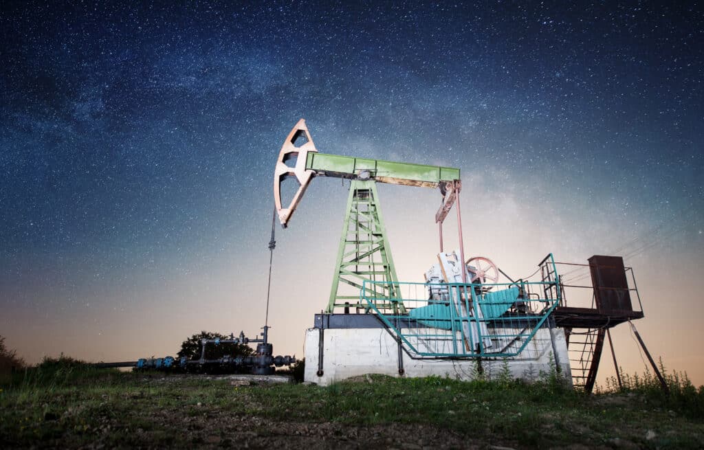 Green oil pump is working on the oil field in the evening under night sky with stars. Petroleum industry equipment