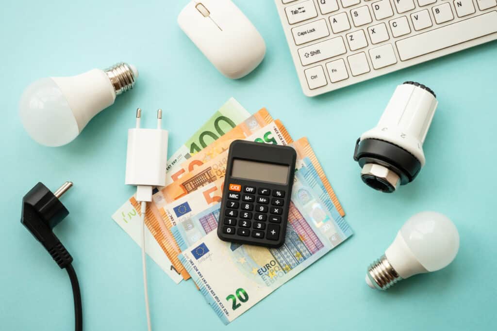 Utility payments. Electricity and heating savings concept. Led lamp, thermostat, calculator, keyboard and electric cable at blue. Top view.