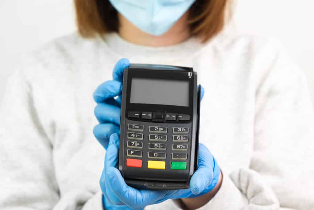 Woman in rubber gloves and face mask holding a POS terminal for payment during pandemic of coronavirus.
