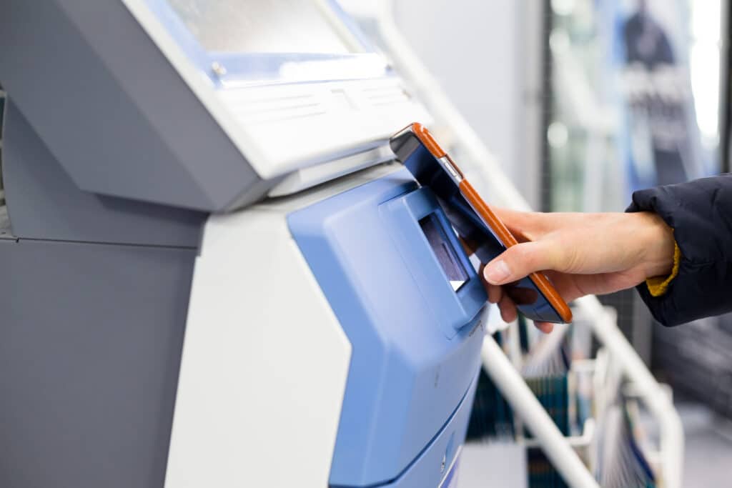 Woman using smartphone for scanning on ticketing machine by NFC