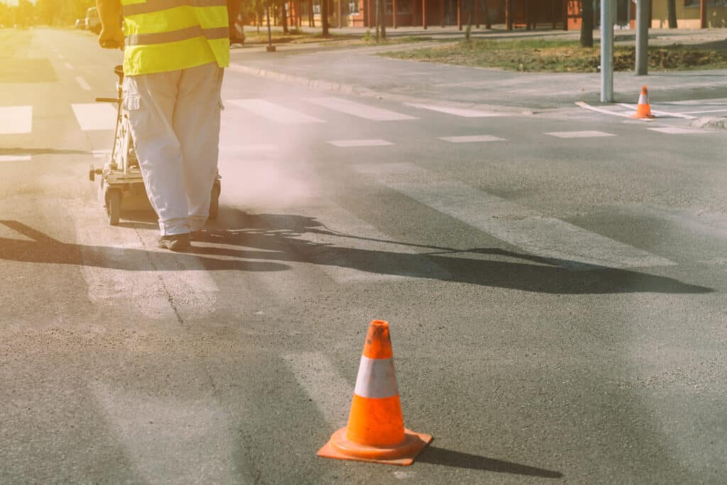 Worker is painting zebra pedestrian crosswalk lines on asphalt surface