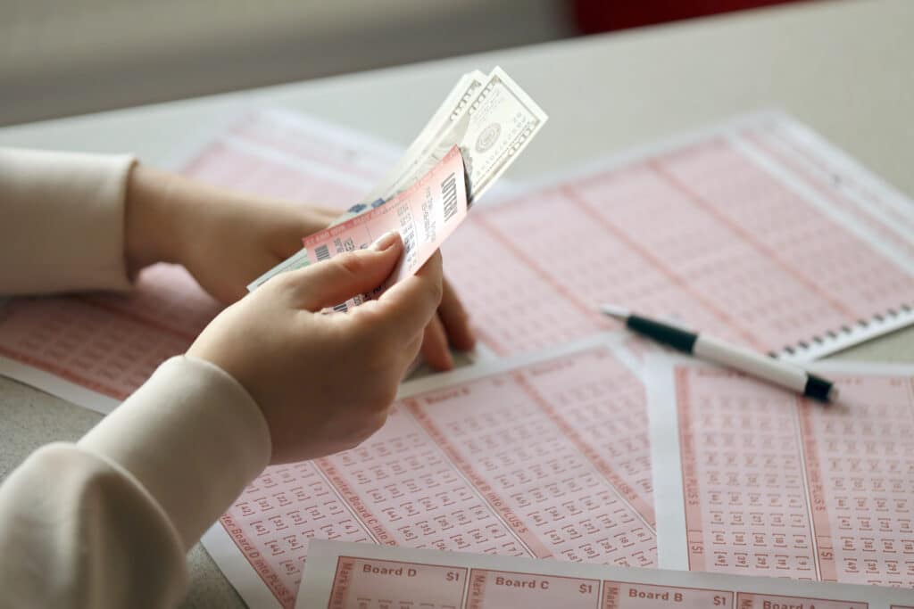 A young woman holds the lottery ticket with complete row of numbers and dollar bills on the lottery blank sheets background. Lottery winner concept