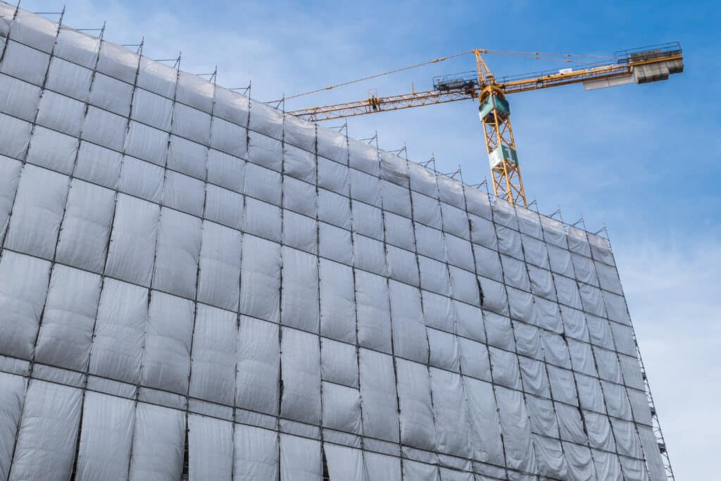 Building facade renovation with cellophane as protection and crane, against a blue sky with white clouds.