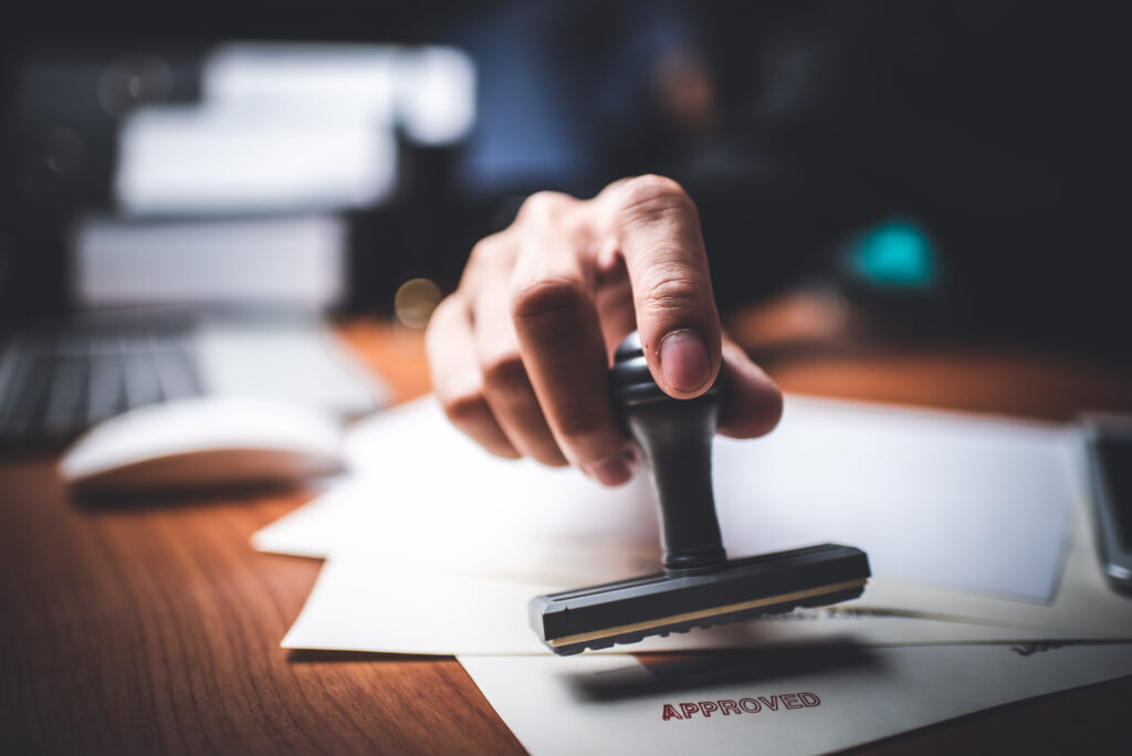 Close-up Of A Person's Hand Stamping With Approved Stamp On Text Approved Document At Desk, Contract Form Paper