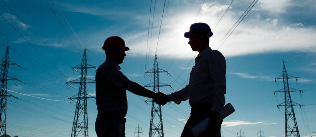 silhouette of engineers standing at electricity station shaking hands