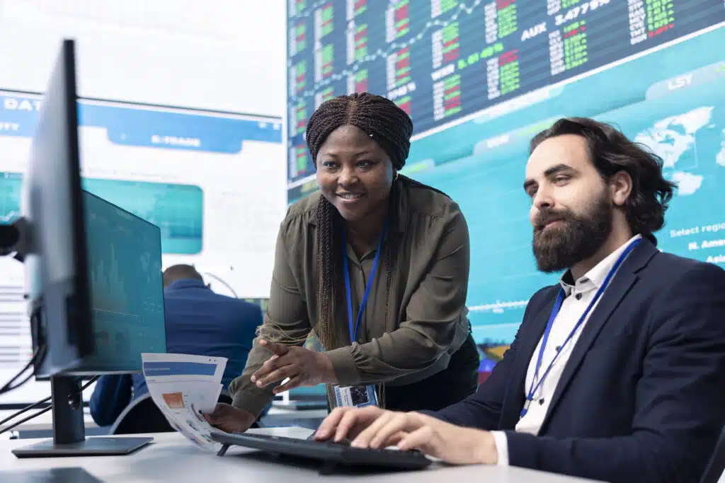 Team of diverse specialists review monthly cost and revenue elements on a computer, creating a financial projection for future improvements and success within the international organization.