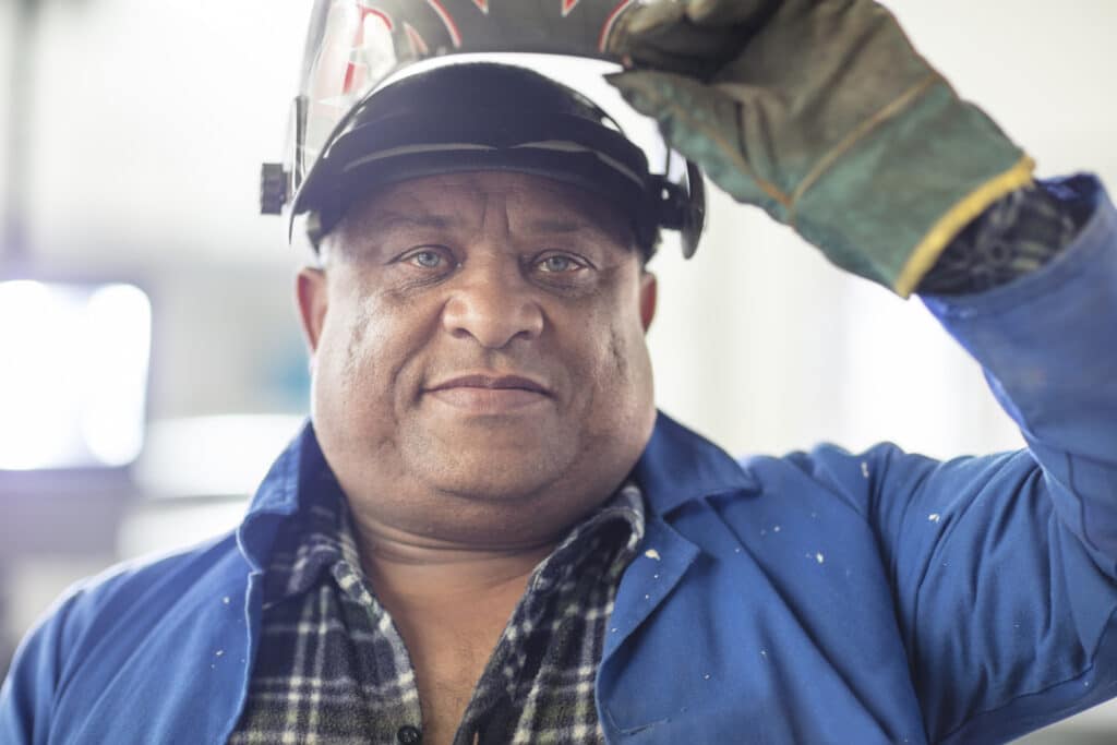 Welder in helmet and work attire smiling at the camera