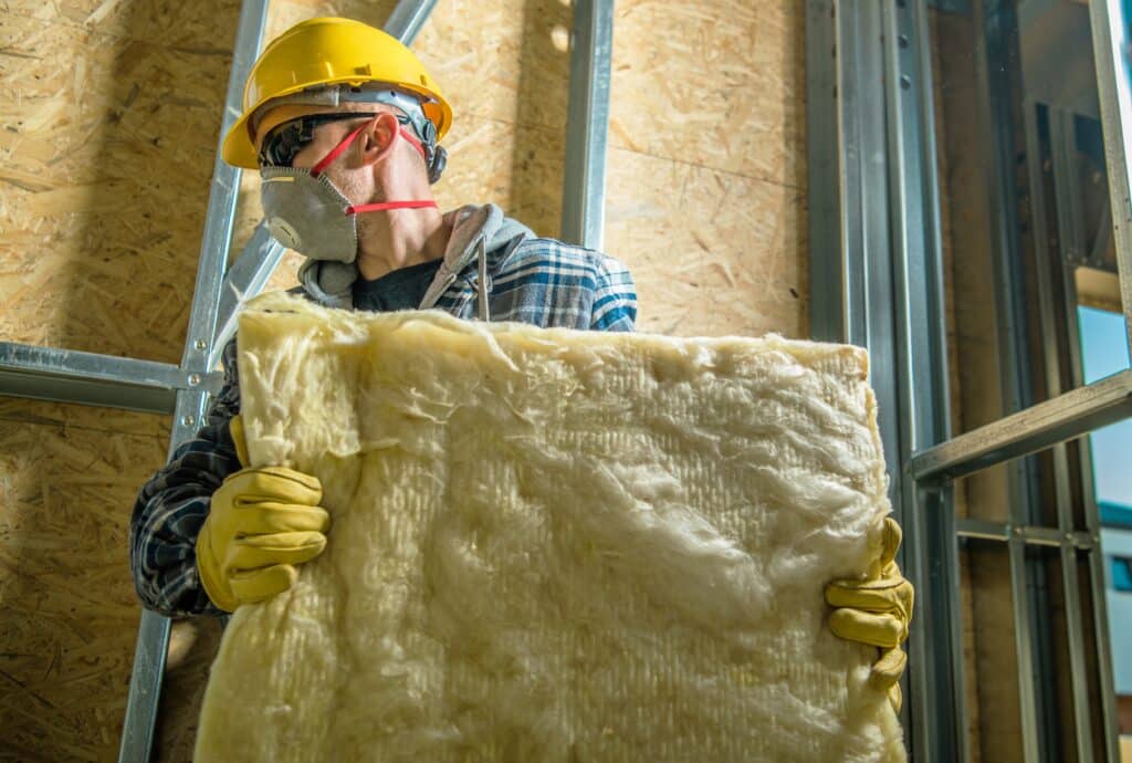 Caucasian Construction Worker Wearing Safety Mask Moving Pieces of Mineral Wool Insulation.