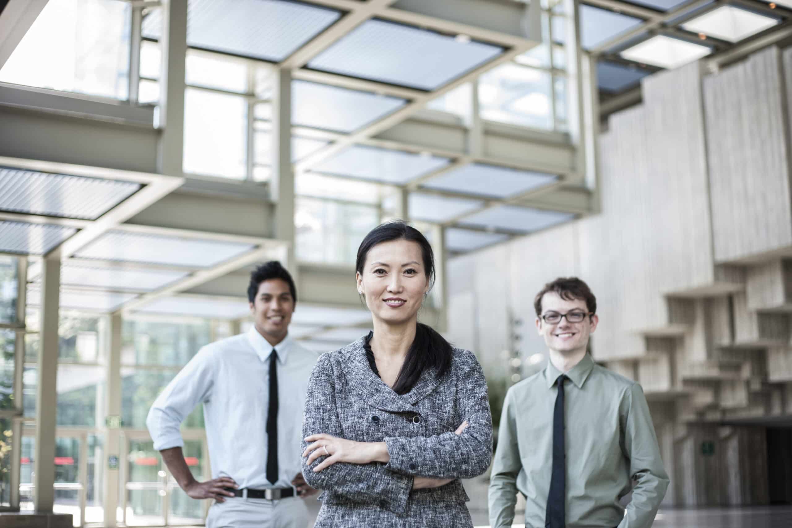 A portrait of a mixed race team of business people standing in the lobby area of a convention center with an Asian businesswoman in the lead.