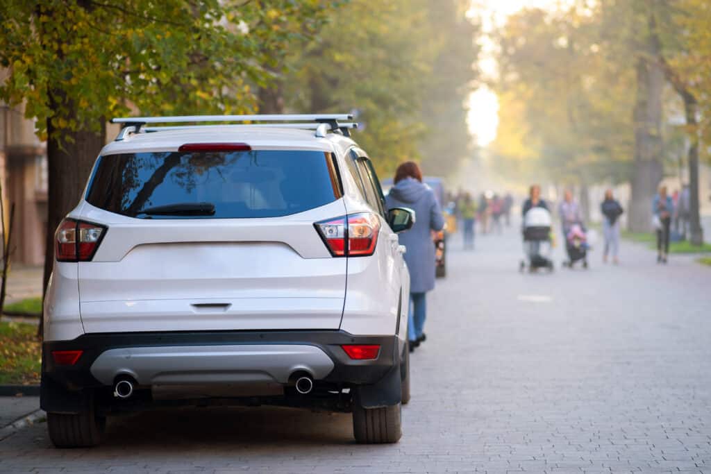 Car parked on a city street side on bright autumn day with blurred people walking on pedestrian zone.