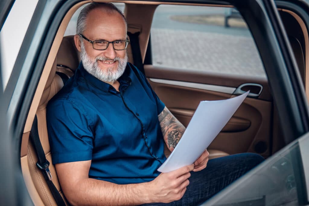 Shot of successful elderly man executive with papers sitting inside of car.