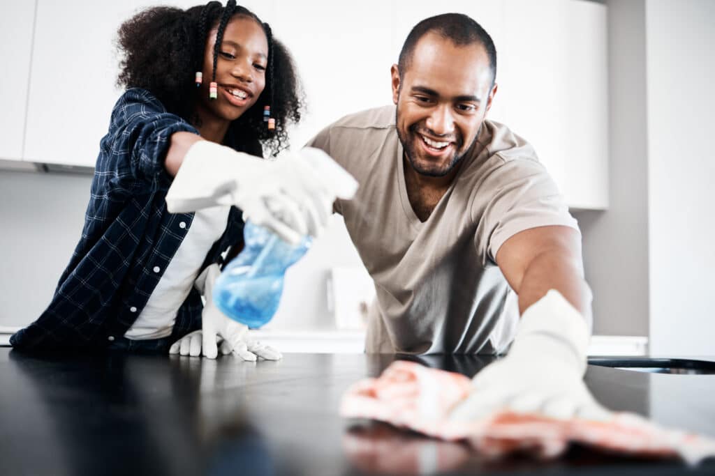 Shot of a young girl helping her father clean the kitchen counter at home.
